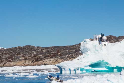 Två säljägare i en båt, med gevär på ryggen. Bakom isberget skymtar MS Fram.